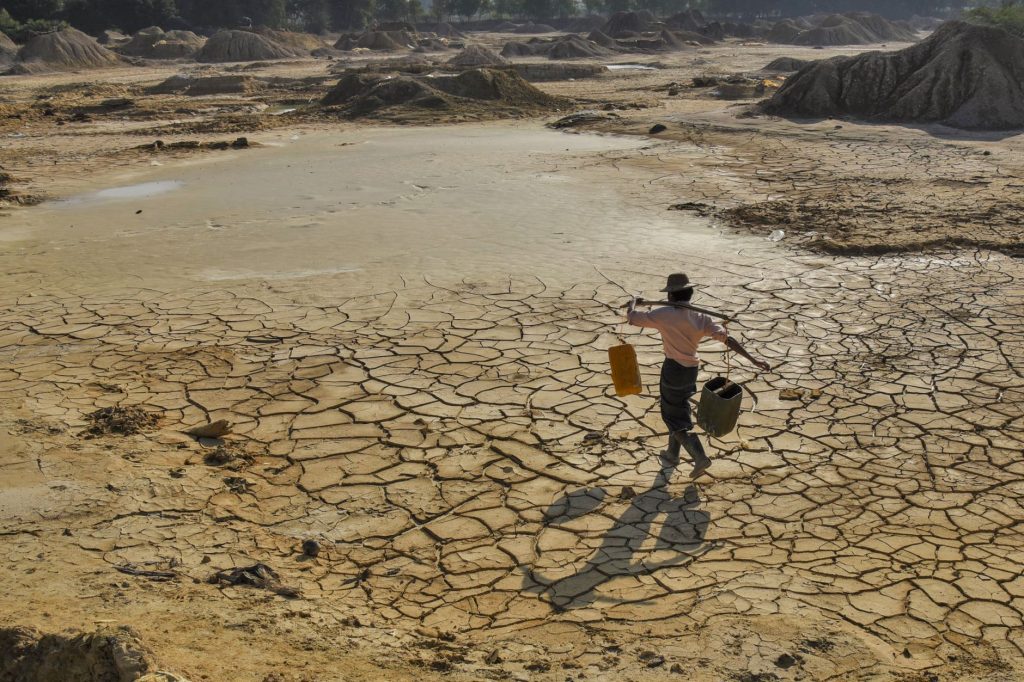 Home - pexels photo 34078646 man carrying water on cracked dry land in myanmar