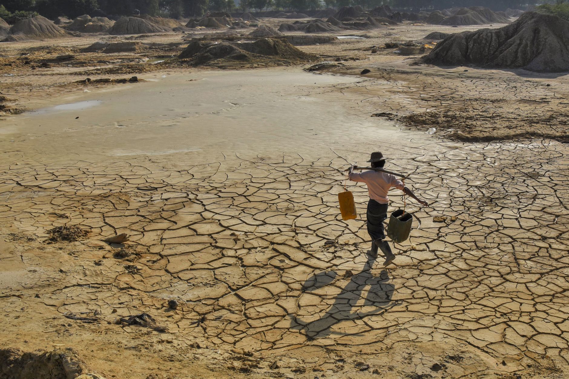 man carrying water on cracked dry land in myanmar